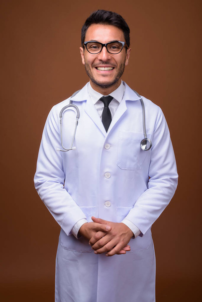 młody przystojny Latynos mężczyzna lekarz na brązowym tle - Zdjęcie, obraz
