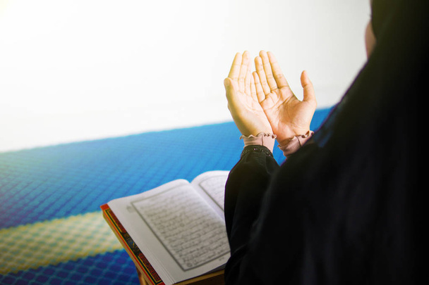 Young muslim woman praying to Allah with hands up in front of The Holy Quran inside a mosque - Foto, imagen