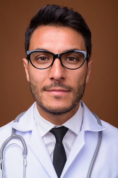 Joven guapo hispano hombre doctor contra marrón fondo - Foto, imagen