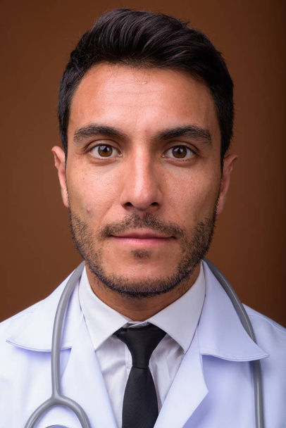Joven guapo hispano hombre doctor contra marrón fondo - Foto, imagen