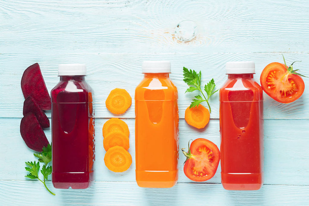 Fresh juice smoothies from a variety of vegetables carrots apple tomatoes beets in bottles on a wooden blue background. - 写真・画像