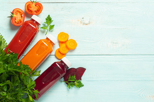smoothies de jus frais d'une variété de légumes carottes pommes tomates betteraves en bouteilles sur un fond bleu en bois
. - Photo, image