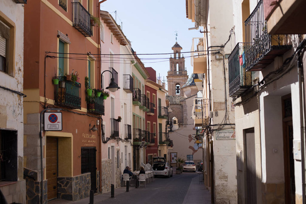 Finestrat, Alicante, Spain - February 23, 2019: Narrow street in the old town with colored houses with worn plaster overlooking the square with the church - 写真・画像