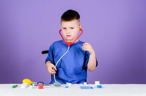 Kid little doctor sit table with stethoscope and medical tools. Medicine concept. Health care. Medical examination. Medical education. Play game. Boy cute child future doctor career. Healthy life - Zdjęcie, obraz