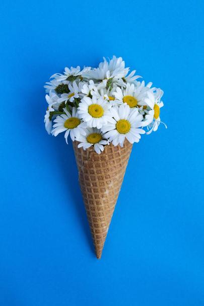 Ice cream cone with chamomiles  in the center of the blue background.Top view.Copy space.Spring or summer flowers concept. - Fotó, kép