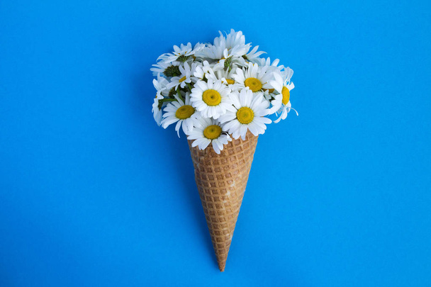 Ice cream cone with chamomiles  in the center of the blue background.Top view.Copy space.Spring or summer flowers concept. - Photo, Image