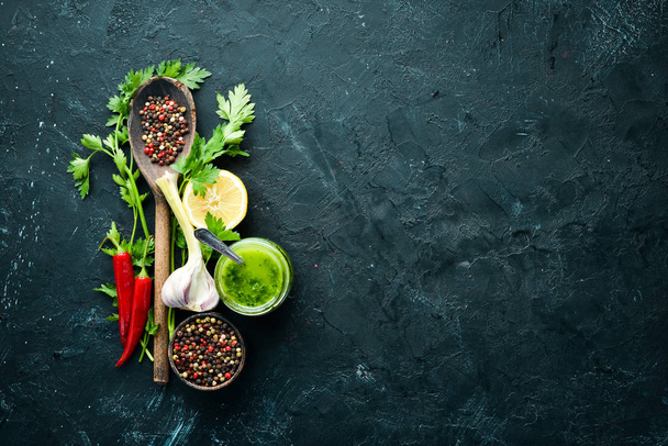 Green parsley sauce, olive oil and spices. Ingredients for chimichurri sauce. On a black background. Top view. free space for your text. - Zdjęcie, obraz