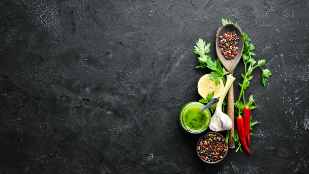 Green parsley sauce, olive oil and spices. Ingredients for chimichurri sauce. On a black background. Top view. free space for your text. - Foto, immagini