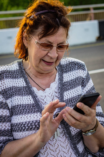 Oude vrouw in glazen met mobiele telefoon op straat - Foto, afbeelding