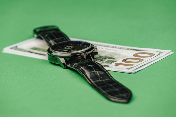 наручные часы лежат на стодолларовой купюре на зеленом фоне
 - Фото, изображение