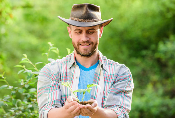 Eco farm worker. Earth day. farming and agriculture cultivation. Gardening. happy earth day. Eco living. muscular ranch man in cowboy hat care plants. successful farmer hold plant in ground in hands - Photo, image