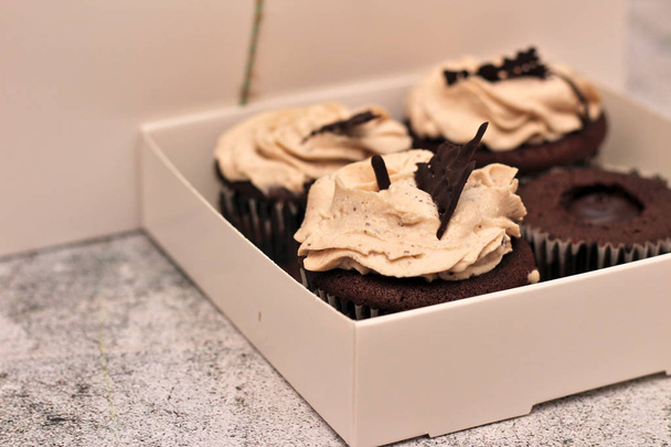 beaux cupcakes recouverts de crème au chocolat dans une boîte blanche attachée avec une corde sur un fond de béton
 - Photo, image