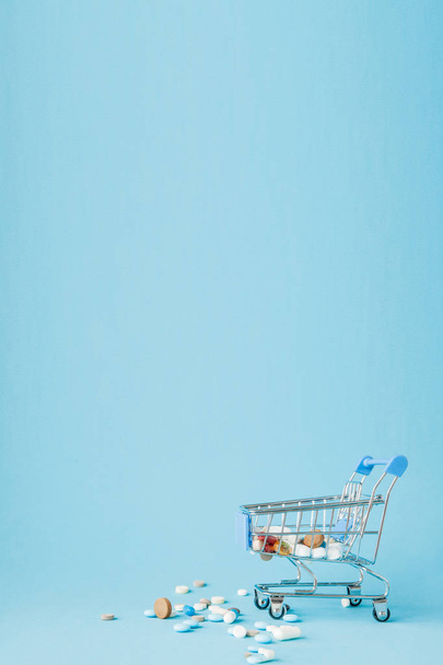Pills and Shopping trolley on blue background. Creative idea for health care cost, drugstore, health insurance and pharmaceutical company business concept. Copy space - Foto, imagen