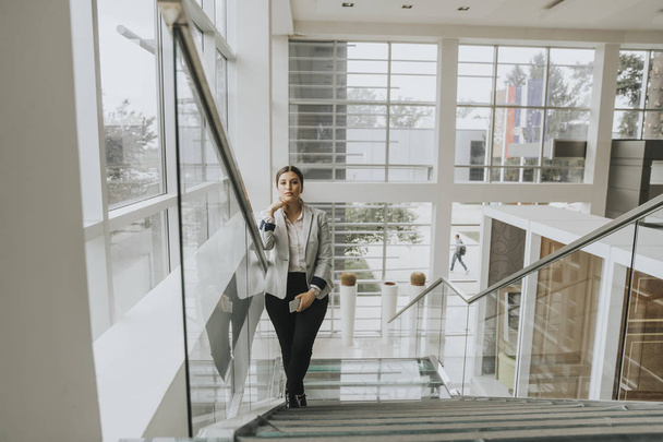 Pretty young business woman stands on the stairs at the office and use mobile phone - Фото, изображение