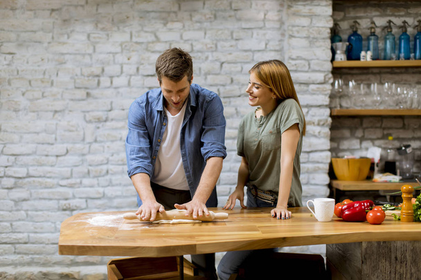 Young couple caking pizza in rustic kitchen together - Photo, Image