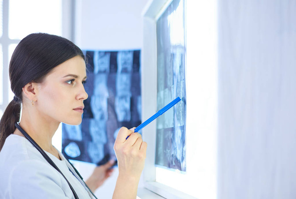 Young smiling female doctor with stethoscope pointing at X-ray at doctors office - Фото, зображення