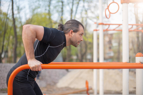 handsome man in the summer outdoors on the sports ground doing an exercise on the uneven bars - Photo, image