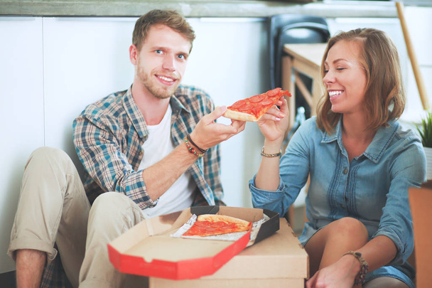 Young couple have a pizza lunch break on the floor after moving into a new home with boxes around them - Foto, Imagem