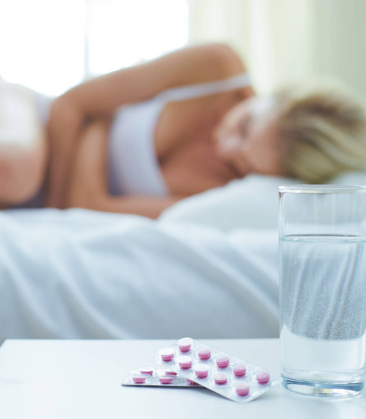 Νεαρή όμορφη γυναίκα με χάπια ξαπλωμένη στο κρεβάτι στην κρεβατοκάμαρα - Φωτογραφία, εικόνα