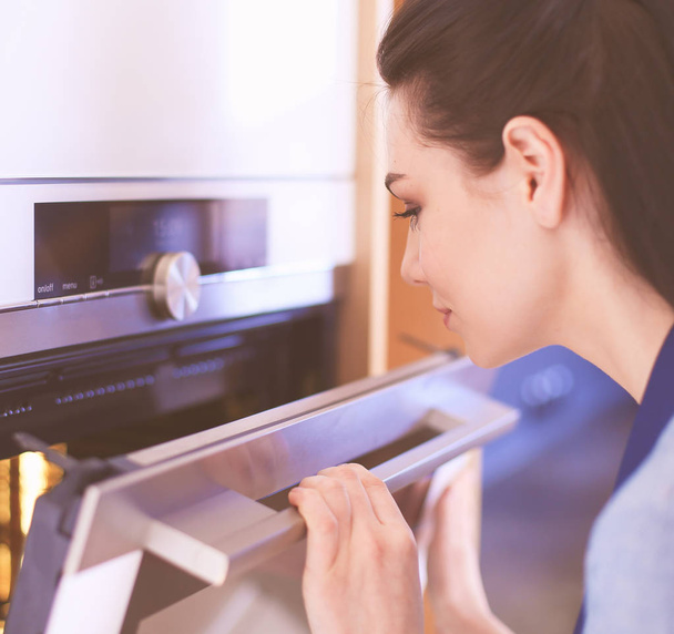 Beautiful young woman checking how her cake is doing in the oven - Foto, Bild