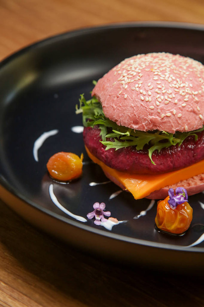 Cena informal fina: hamburguesa vegana rosa servida en el plato negro decorado con flores comestibles
 - Foto, Imagen