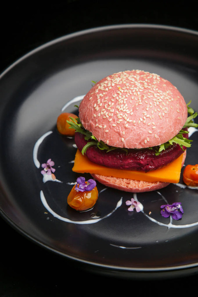 Cena informal fina: hamburguesa vegana rosa servida en el plato negro decorado con flores comestibles
 - Foto, imagen