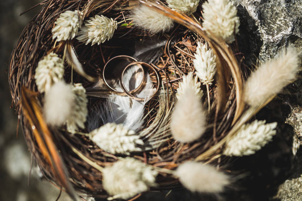 Dois anéis de casamento em ninho de vime artesanal com flores silvestres secas
 - Foto, Imagem