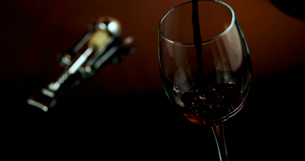 Close-up van rode wijn gegoten in wijn glas. Vleugel kurkentrekker naast wijn glas. 4k - Video