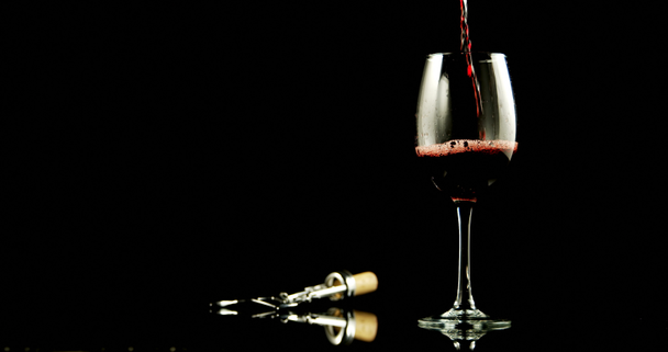 Close-up of red wine poured in wine glass against black background. Wing corkscrew beside wine glass. 4k - Filmagem, Vídeo