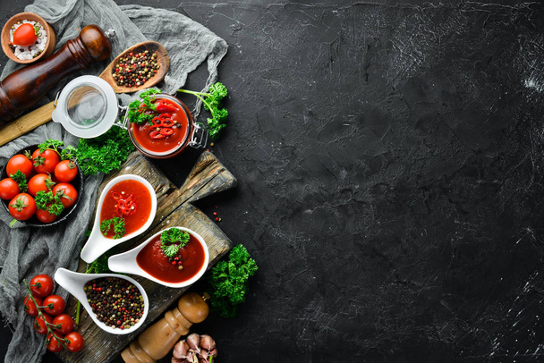 A set of tomato sauces on a black stone background. Ketchup, barbecue sauce, tomato sauce. Top view. Free space for your text. - Foto, Imagen