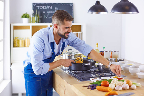 Усміхнений і впевнений шеф-кухар стоїть на великій кухні
 - Фото, зображення