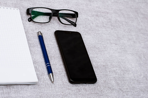 Blank notepad with blue pen and smartphone and glasses flat lay. View on stationery with mobile phone and spectacles. Art, business, creation, imagination, office supplies and business concept. Contain empty space for your design or montage. - Zdjęcie, obraz