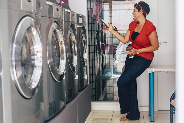 Woman using smartphone at laundry mat automatic service shop - 写真・画像