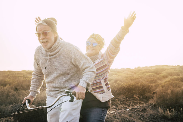 Ευτυχία για ενεργούς ηλικιωμένους συνταξιούχους έννοια του τρόπου ζωής - χαρά ηλικιωμένο ζευγάρι ιππασία μαζί ένα ποδήλατο γέλιο και χαμογελώντας πολύ και διασκεδάζοντας - Φωτογραφία, εικόνα