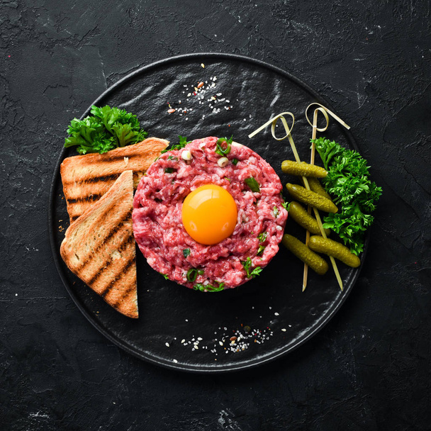 Beef steak tartare with raw egg yolk, pickled cucumber and onions. French cuisine. Top view. Free space for your text. - Fotó, kép
