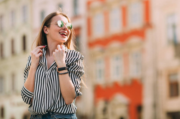 Όμορφη νεαρή γυναίκα με γυαλιά ηλίου που περπατούν στην πόλη. Χαμόγελο. - Φωτογραφία, εικόνα