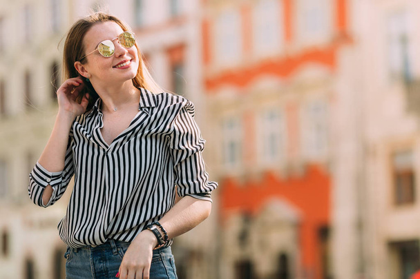 schöne junge Frau mit Sonnenbrille, die durch die Stadt spaziert. Lächeln. - Foto, Bild