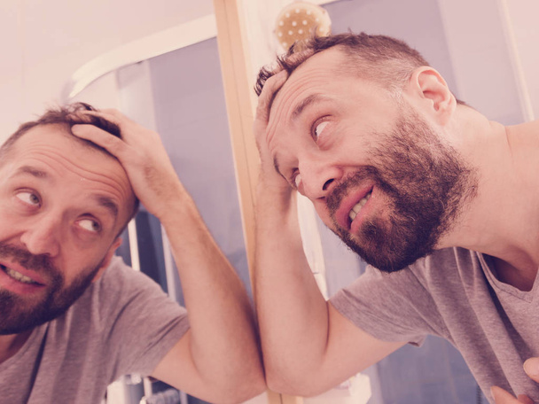 glücklicher erwachsener Mann, der Haare im Spiegel betrachtet - Foto, Bild