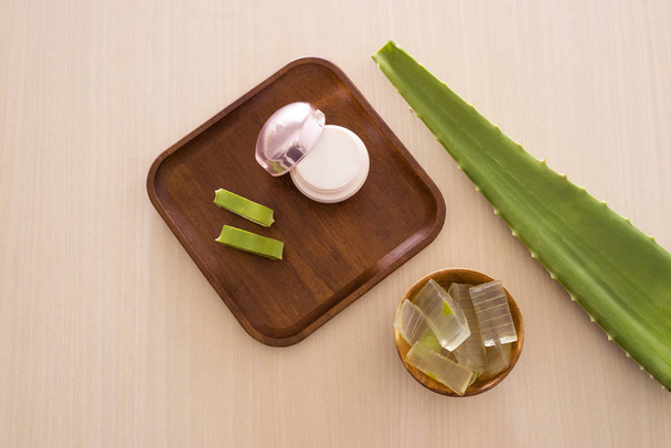 Aloe vera cosmetic cream on wooden tray with aloe leave and bowl on light background. - Foto, imagen