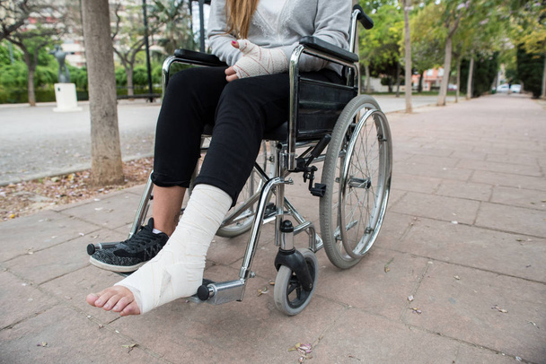 Person injured in a wheelchair. Foot and hand bandages, outdoor photography in a park - Photo, Image