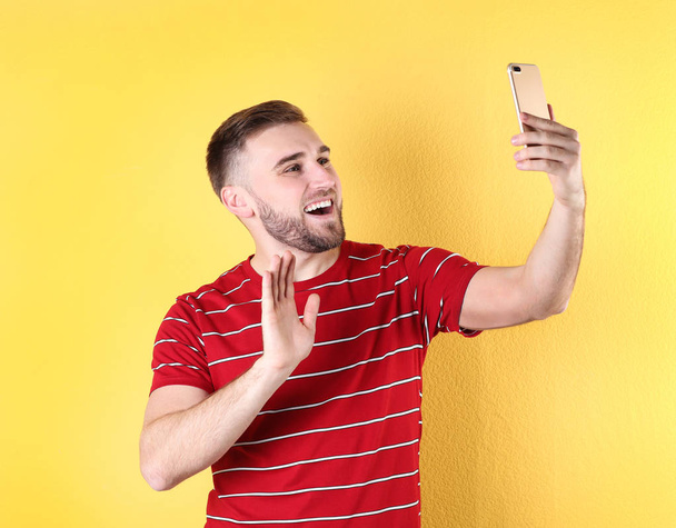 Junger Mann nutzt Video-Chat auf Smartphone vor farbigem Hintergrund - Foto, Bild