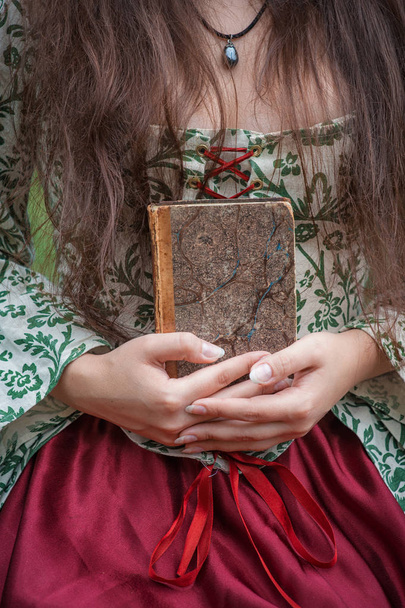 Hands of woman in medieval dress holding old vintage book - Fotó, kép