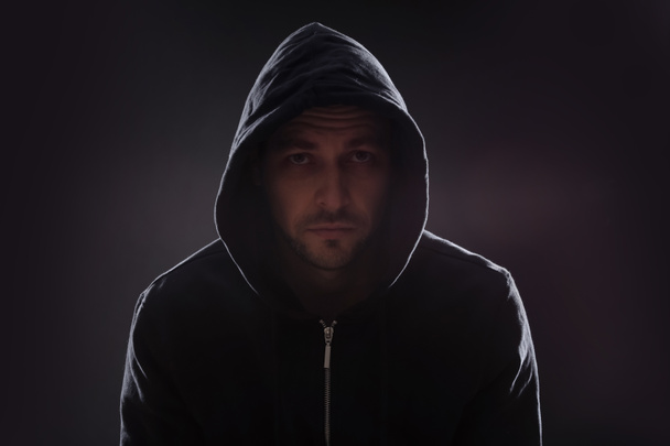 Mysterious man in hoodie on dark background. Dangerous criminal - Zdjęcie, obraz