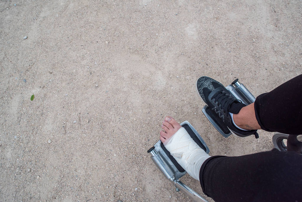 Pessoa ferida numa cadeira de rodas. Ligaduras de pé e mão, fotografia ao ar livre em um parque
 - Foto, Imagem