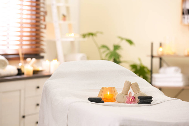 Composition with herbal bags, candle and stones on massage table in spa salon. Space for text - Photo, Image