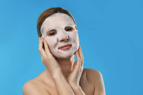 Beautiful woman with cotton mask sheet on face against color background - Foto, afbeelding