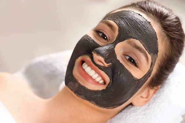 Beautiful woman with black mask on face relaxing in spa salon, closeup - Foto, imagen