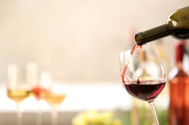 Pouring red wine from bottle into glass on blurred background. Space for text - Foto, Bild