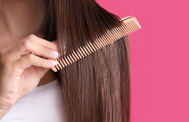 Young woman with wooden hair comb on color background, closeup. Space for text - 写真・画像