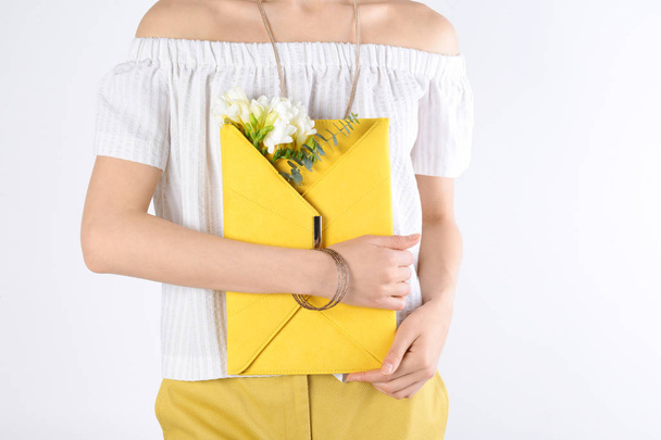 Stylish woman with clutch and spring flowers against light background, closeup - Valokuva, kuva
